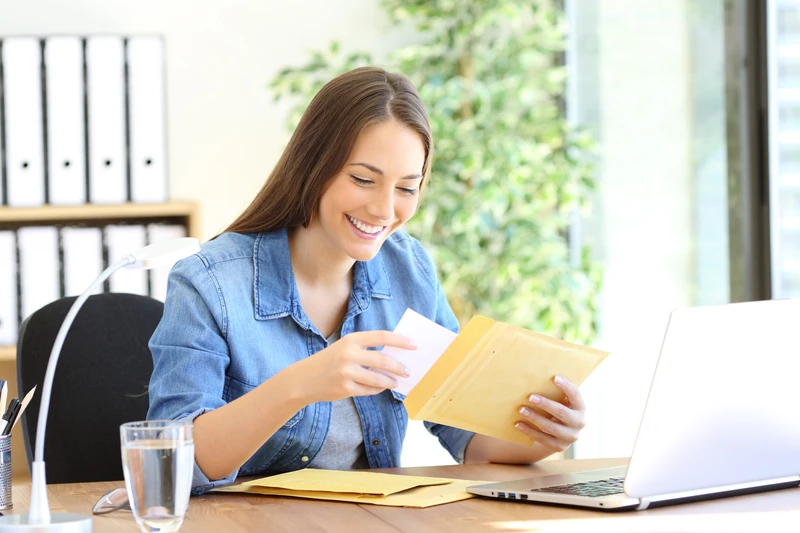Happy entrepreneur putting document in an envelope working at office